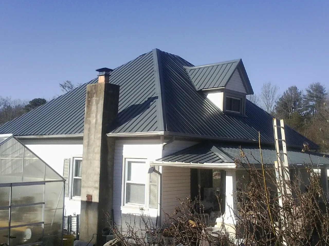 Dark blue standing seam metal roof on a white farmhouse with dormer — Slate & Tile Roof Repair by Roofing Brothers in Center Hill