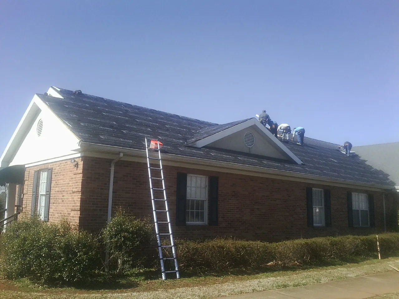 Crew tearing shingles off a brick ranch roof with a ladder set — Emergency Roof Repair work by our crew in Center Hill