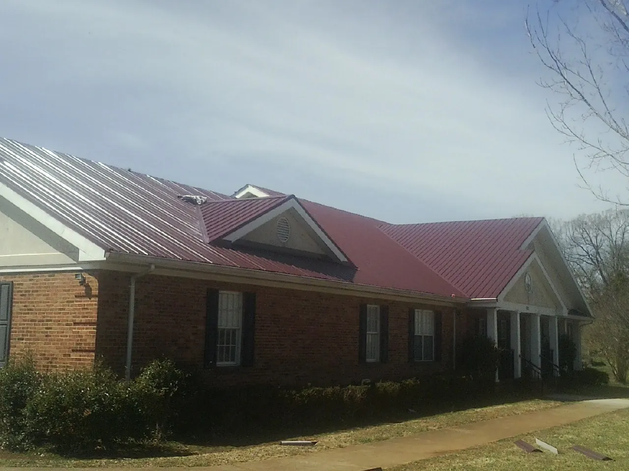 Red metal roof with gabled entries on a long brick building, from a Hail Damage Roof Repair job in Center Hill