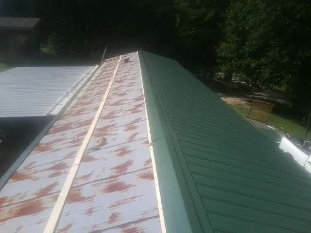 Old rusted panels beside newly installed green metal roofing — Wind Damage Roof Repair by Roofing Brothers in Center Hill