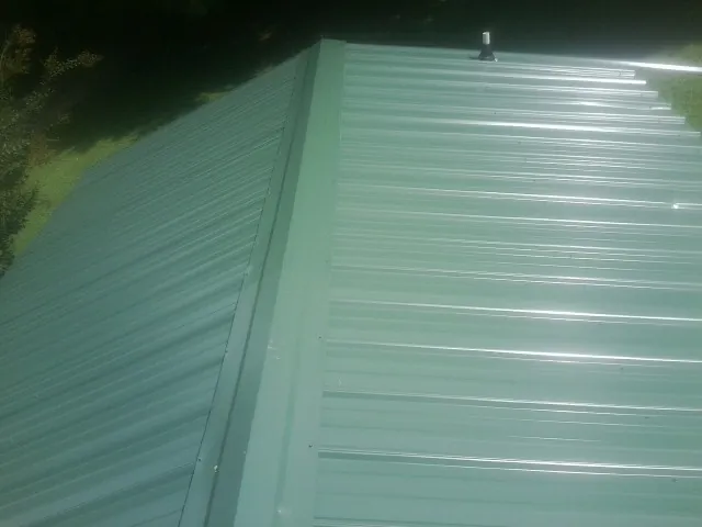 New green metal panels meeting at the ridge of a roof — Flat Roof Repair work by our crew in Center Hill