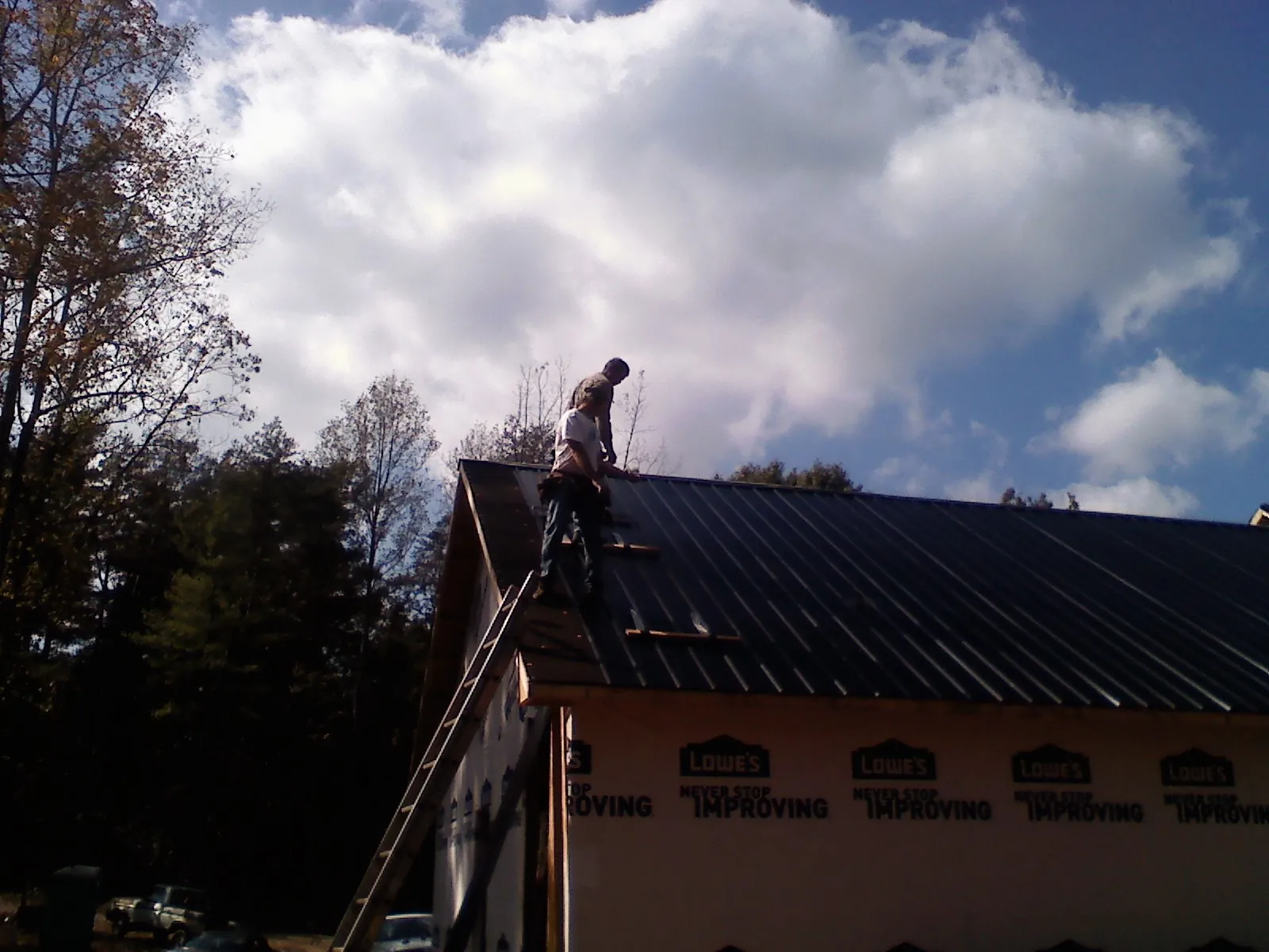 Roofer fastening dark metal panels high against a cloudy sky, from a Roof Inspection job in Center Hill
