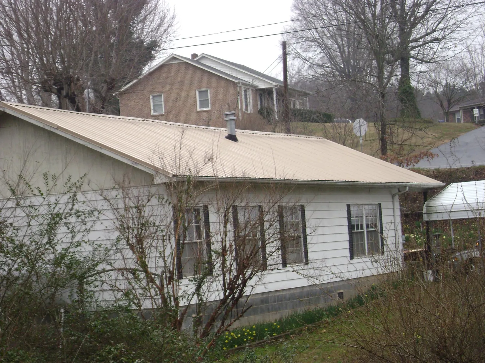 Tan metal roof on a white sided house set into a hillside — Commercial Roofing by Roofing Brothers in Center Hill