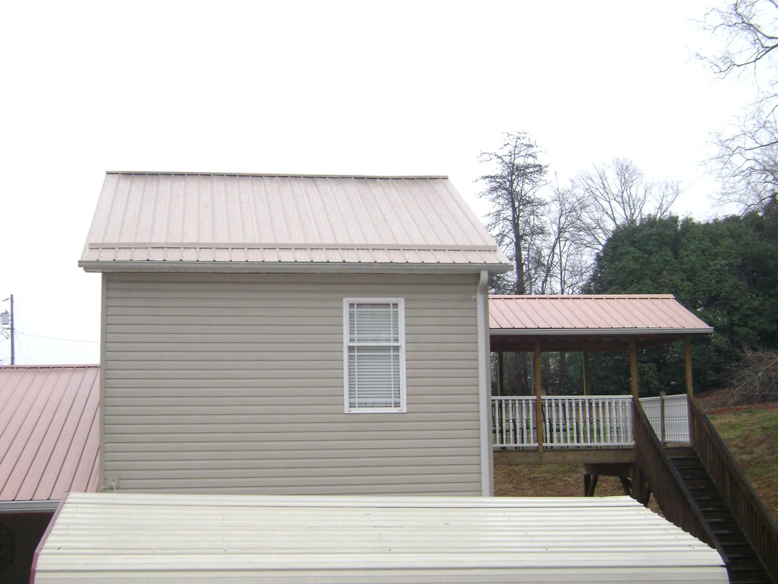 Tan metal roofs on a two story addition and attached porch, from a Roof Replacement job in Center Hill